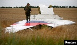 Separatis pro-Rusia bersenjata berdiri di bagian reruntuhan pesawat Malaysia Airlines Boeing 777 setelah jatuh di dekat pemukiman Grabovo di wilayah Donetsk, 17 Juli 2014. (Foto: Reuters)