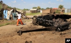FILE - A man walks past the remains of a tank destroyed during fighting between government and rebel forces in the Jebel area of the capital, Juba, South Sudan, July 16, 2016.