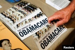 FILE - A Tea Party member reaches for a pamphlet titled "The Impact of Obamacare," at a Tea Party rally in Littleton, New Hampshire, Oct. 27, 2012.