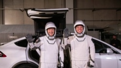 In this Friday, Jan. 17, 2020 photo made available by NASA, astronauts Doug Hurley, left, and Robert Behnken pose in front of a Tesla Model X car during a SpaceX launch dress rehearsal at Kennedy Space Center in Cape Canaveral, Fla. (Kim Shiflett/NASA)