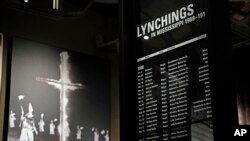 In this Nov. 10, 2017 image, a monolith listing the names, dates and rationale for the lynching of African-American residents rests in the foreground of a photograph of a burning Ku Klux Klan cross on display in the Mississippi Civil Rights Museum.