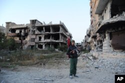 FILE - A civilian fighter holding the Libyan flag stands in front of damaged buildings in Benghazi, Libya, Feb. 23, 2016.