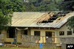 FILE - A woman stands outside the damaged roof of a school's dormitory, after it was set on fire, in Bafut, in the northwest English-speaking region of Cameroon, Nov. 15, 2017.