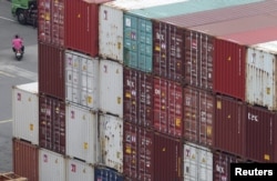 FILE - A man rides a scooter near containers at Keelung port, northern Taiwan, Oct. 30, 2015.
