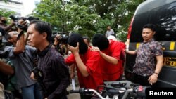 FILE - A plainclothes policeman holds a rifle as he escorts suspects during a police investigation into a men's club after a weekend raid on what authorities described as a "gay spa" in Jakarta, Indonesia, Oct. 9, 2017.
