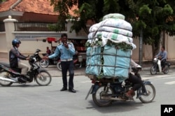 A Cambodian man, right, drive his motorbike overloaded with vegetable sacks as he passes a traffic police officer, center, in Phnom Penh, Cambodia, Tuesday, Aug. 25, 2015. (AP Photo/Heng Sinith)