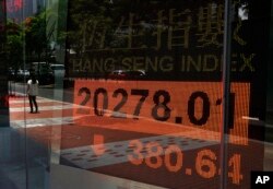 A woman walks past a bank electronic board showing the Hong Kong share index outside a Hong Kong local bank, July 3, 2013.