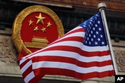 FILE - An American flag is flown next to the Chinese national emblem during a welcome ceremony for visiting U.S. President Donald Trump outside the Great Hall of the People in Beijing, Nov. 9, 2017.