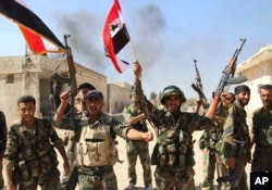In this photo taken on Oct. 11, 2015, Syrian soldiers waving Syrian flags celebrate the capture of Achan, Hama province, Syria.