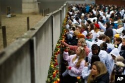 FILE - People put flowers in the remains of the Berlin Wall during a commemoration ceremony to celebrate the 30th anniversary of the fall of the Berlin Wall at the Wall memorial site at Bernauer Strasse in Berlin, Nov. 9, 2019.