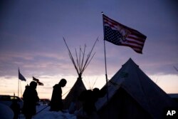 FILE - Travelers arrive at the Oceti Sakowin camp where people have gathered to protest the Dakota Access oil pipeline as they walk into a tent next to an upside-down American flag in Cannon Ball, North Dakota, Dec. 2, 2016.