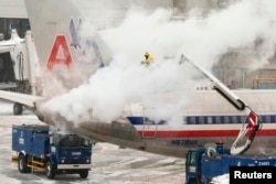 An American Airlines crew member sprays de-icing solution on a plane during a winter nor'easter snow storm in Boston, Massachusetts, Jan. 2, 2014.