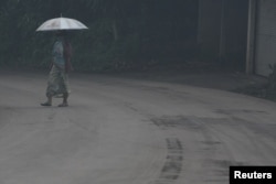 A woman uses an umbrella as she walks through ash from Mount Agung volcano during an eruption in Bebandem Village, Karangasem, Bali, Indonesia, Nov. 26, 2017.