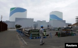 FILE - An employee of Kyushu Electric Power Co walks in front of reactor buildings at the company's Sendai nuclear power plant in Satsumasendai, Kagoshima prefecture.