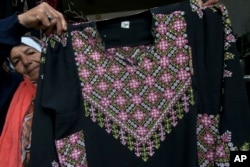 FILE - Samiha Jeheshat, displays a handmade embroidered Palestinian thobe at her showroom in the West Bank village of Idna, north of Hebron, Jan. 28, 2019.
