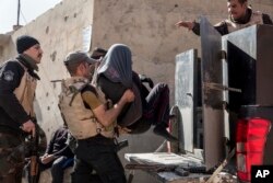 Iraqi security officers place a suspected Islamic State group member into the back of a waiting pickup truck, in east Mosul, Feb. 21, 2017.
