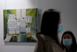 Visitors wearing face masks hang out near an art piece painted by Chinese artist Yang Qian, depicting a hospital reception counter plastered with instructions for patients, as they visit a studio in Wuhan in central China's Hubei province