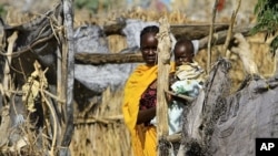 A woman carries her child at her shelter during a visit by Qatar's Minister of State for Foreign Affairs Ahmed Bin Abdullah Al-Mahmoud and UN/AU negotiator and Darfur chief mediator Djibril Bassole to Kalma internally displaced person (IDP) camp outside N