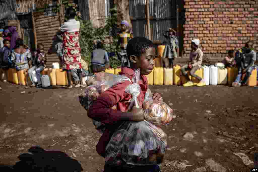 A boy sells snacks as residents queue with their water jars to collect water from a water point in Bukavu, Democratic Republic of Congo.&nbsp;(Photo by Luis TATO / AFP)