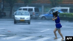 Seorang perempuan menyeberang japan saat human lebat dan angin kyat melanda Haikou, provinsi Hainan di China Selatan (18/7).