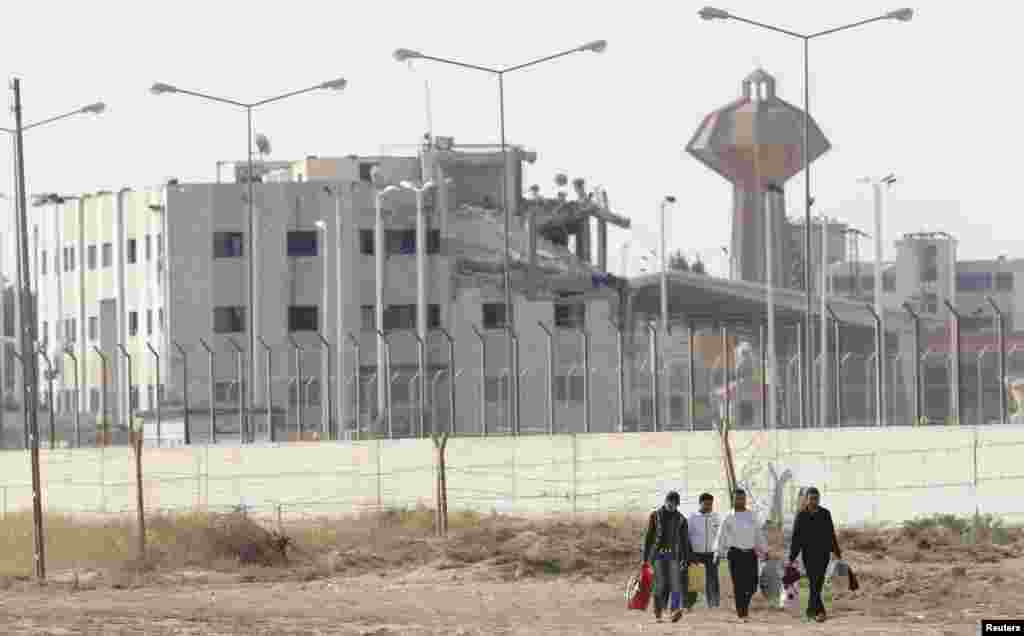 The damaged Syrian Tel Abyad custom office is seen in the background, as Syrian men walk from Syria to Turkey after crossing the fence next to the Akcakale border gate, in southern Sanliurfa province October 4, 2012.