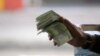 FILE - A Tunisian illegal black market money changer clutches a fistful of Dinars in the town of Ben Guerdane, near the Libyan border, April 16, 2019.