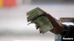 FILE - A Tunisian illegal black market money changer clutches a fistful of Dinars in the town of Ben Guerdane, near the Libyan border, April 16, 2019.