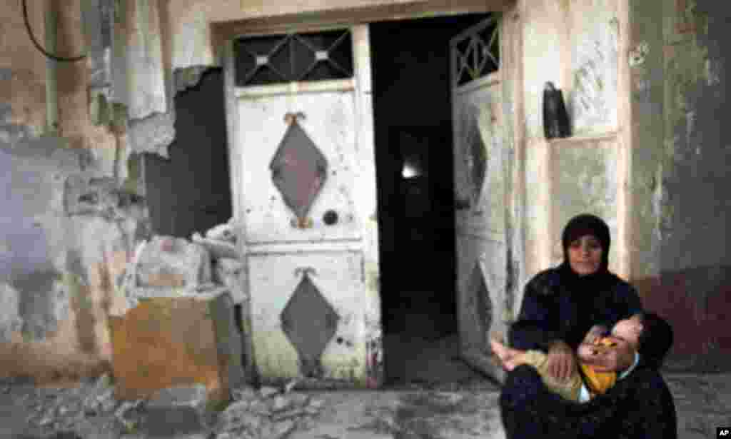 A woman holds a child in front of their destroyed home in Tremseh, Syria about 15 kilometers northwest of Hama, July 14, 2012.